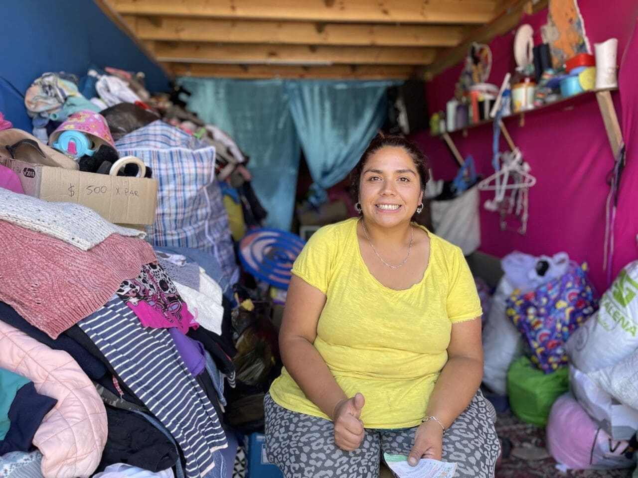 Woman sitting next to pile of clothing she will sell in her home-based shop