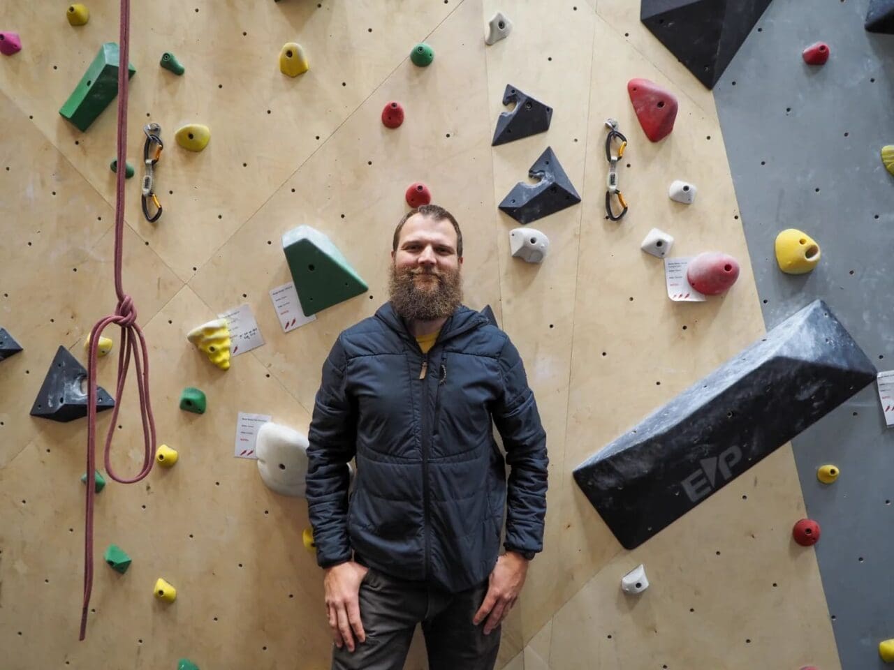 Willie long standing in front of an indoor rock climbing wall