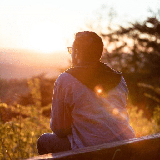 A man sitting on a hill with the bright sun shining on him