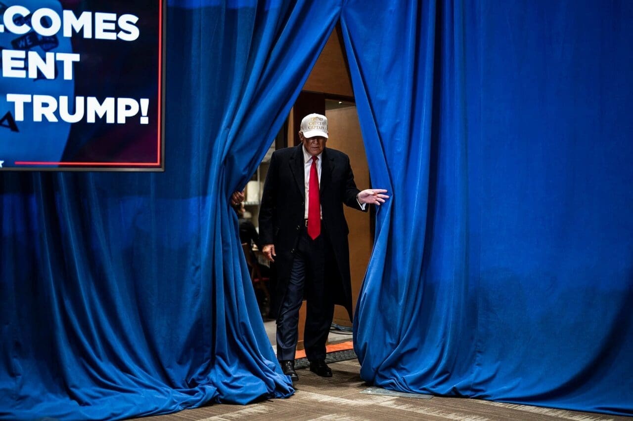 Iowa Trump walking on stage from between blue velvet curtains