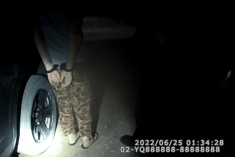 Photo of just the handcuffed hands and legs of woman at police car