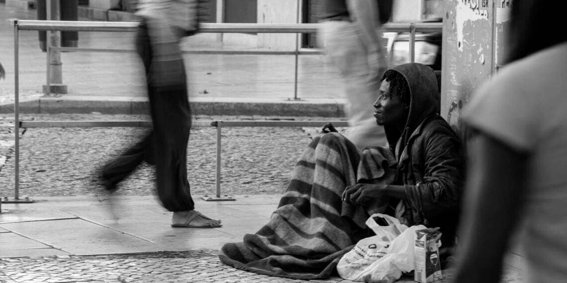 Photograph of a homeless man on the city sidewalk as people rush past black and white photo
