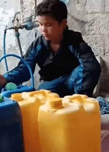 A palestinian chilld fills containers with water from a hose early in the war.