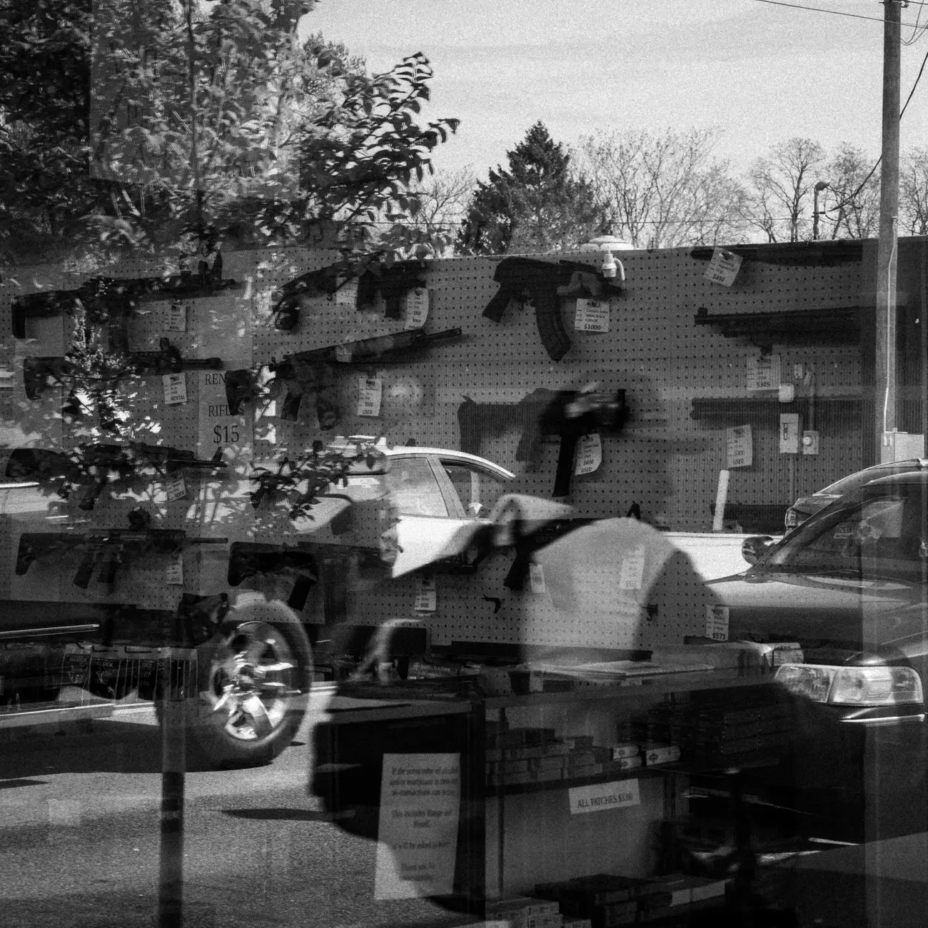 Gun stores: reflection of a man on a bike looking through a gun store window