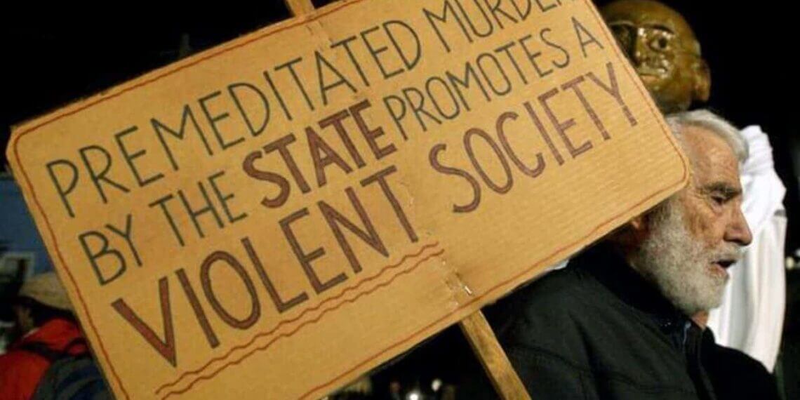 A pro-life protestor with a sign that says “premeditated murder by the state promotes a violent society”