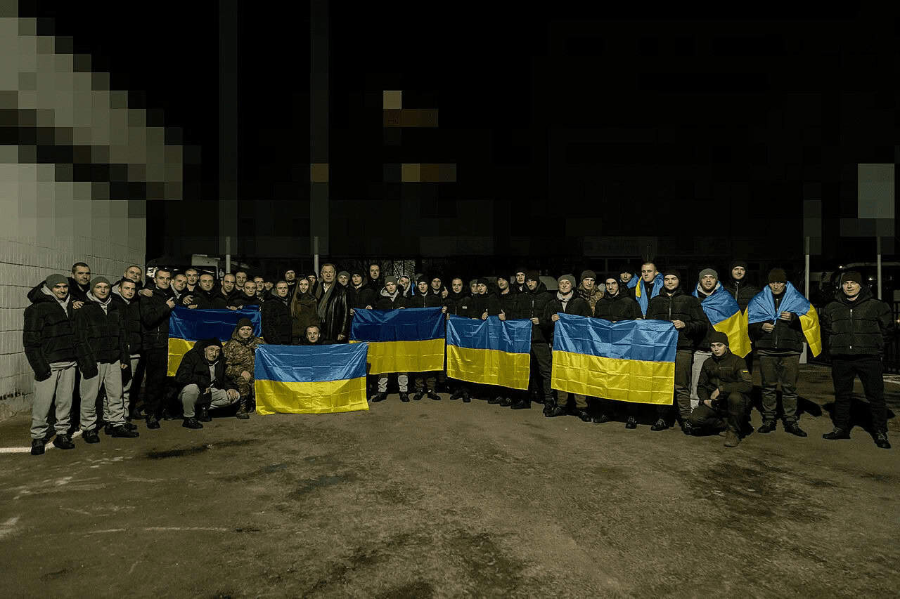 Soldiers in ukraine war following a prisoner swap holding ukrainian flags across the front row