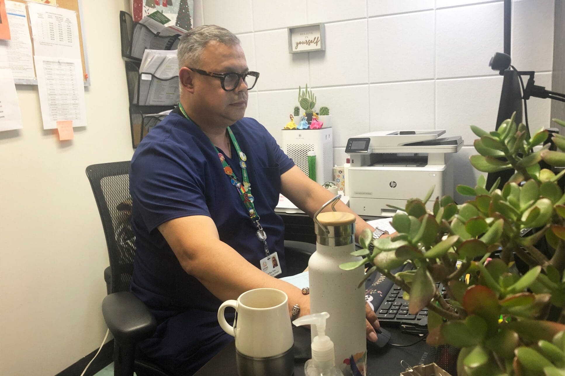 HIV Latinos: A man in blue scrubs works in an office