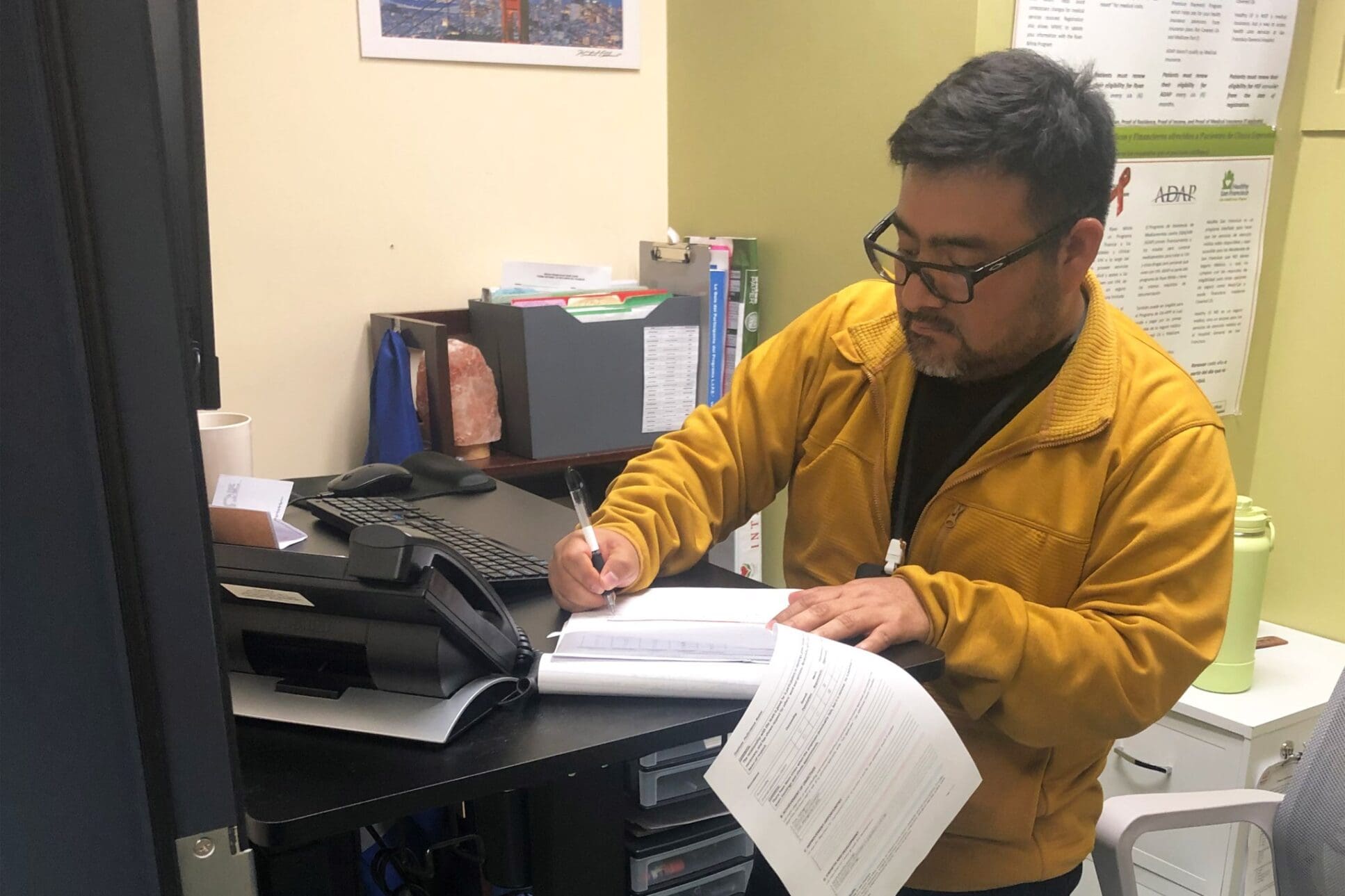 A man in a yellow jacket works in a small office