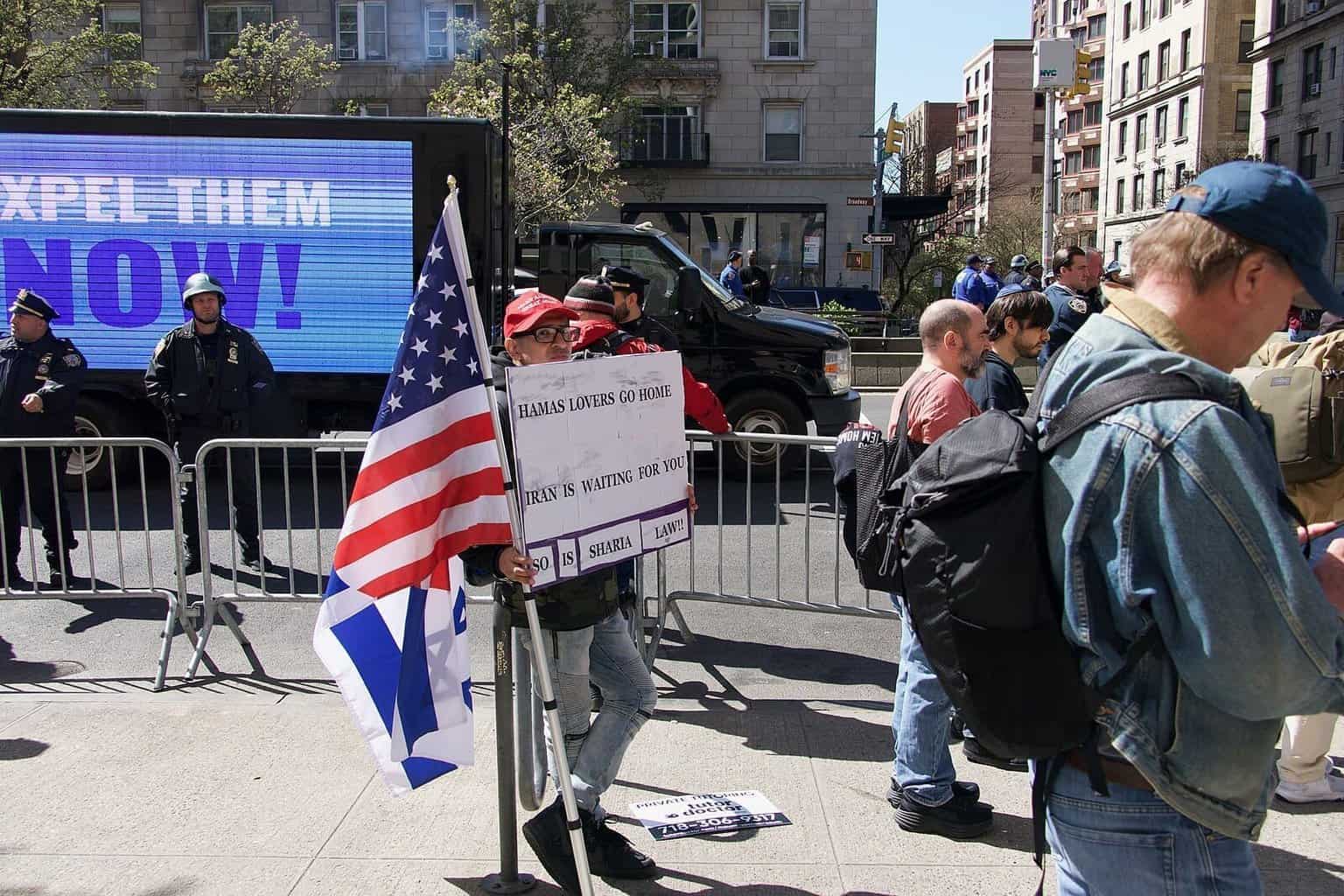 Protests in and around columbia university in support of palestine and against israeli occupation. A pro-israel demonstrator is in a less-populated area holding a sign saying "hamas lovers go home. Iran is waiting for you. So is sharia law! " in the background is a different led truck with a simple message: "expel them now! "