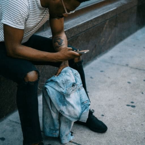 Good news a man sitting on a ledge outdoors looking at his cell phone