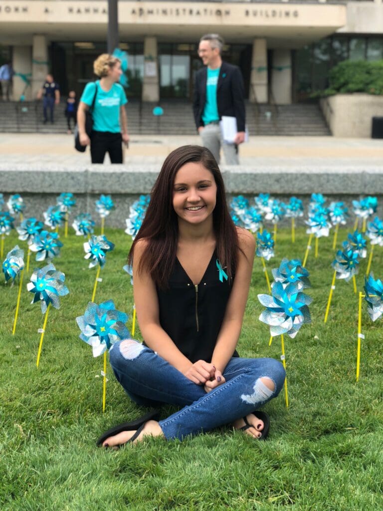  Former gymnast Kaylee Lorincz sits outside the Hannah Administration Building on Michigan State University campus in 2018 surrounded by teal pinwheels placed to represent support for survivors of ex-MSU and Olympic doctor Larry Nassar. 