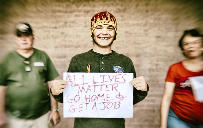 Black Lives Matter anti-protestA young teen in a knit cap with flames on it holds an All Lives Matter sign with his parents or grandparents in the background