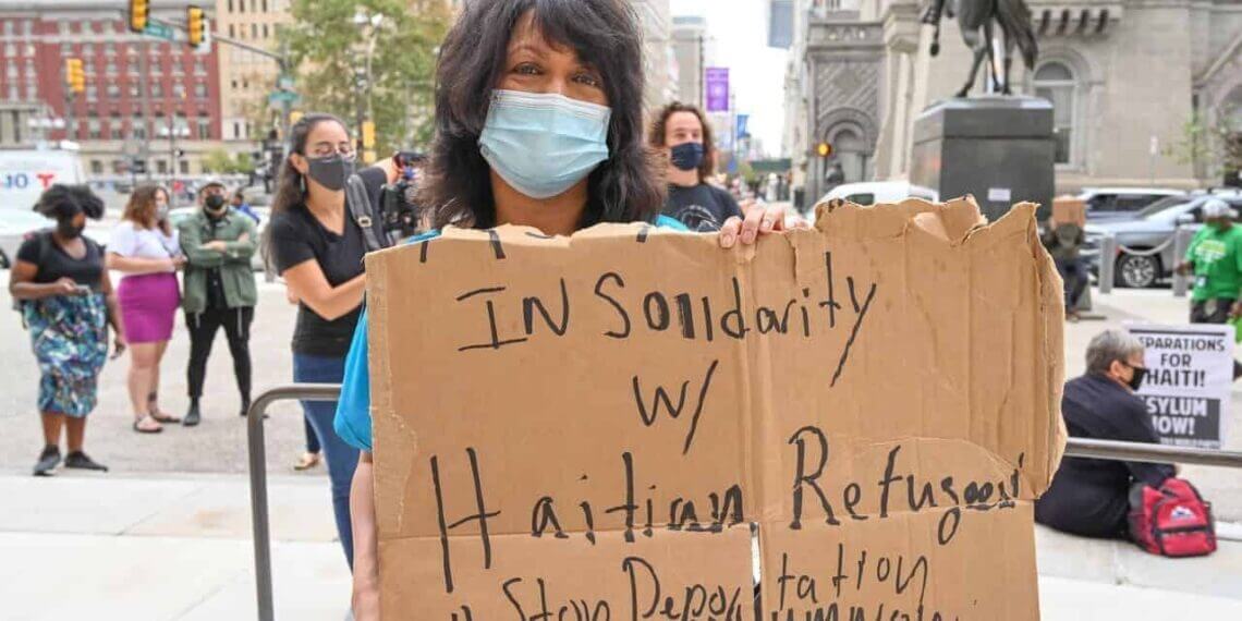 A woman holding a cardboard sign during a protest in philadelphia against deportation of haitian migrants.