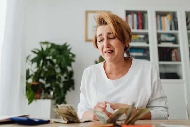 A woman sitting at a table counting money and crying