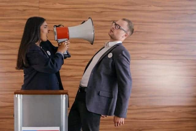 Vote against their own best interests. A female politician yells into a bullhorn in the face of her opponent.