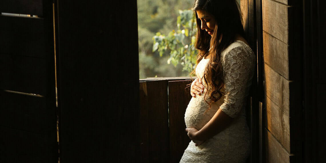 Pregnant woman standing in the sun by a window in a barn