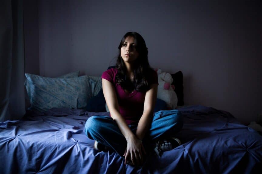 High school student sitting on a bed in her room