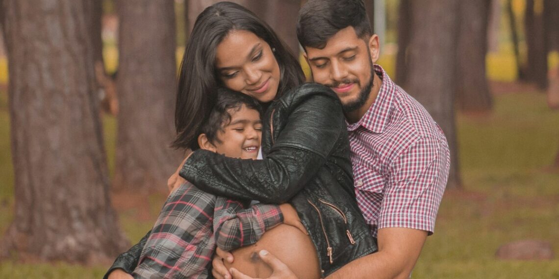 Latino family with husband and small child hugging pregnant woman