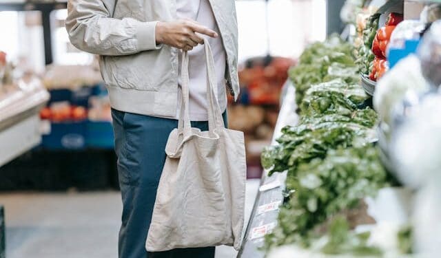 Mass deportation man holding a reusable shopping tote looking at green vegetables in a grocery store.