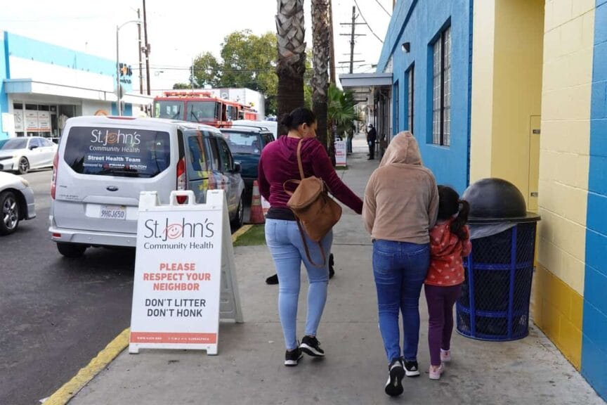 Community health clinic workers prepare to protect families family walking on the sidewalk in front of a city health clinic