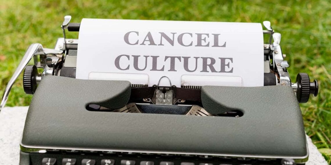 Retro typewriter with 'cancel culture' typed paper on grass background outdoors.