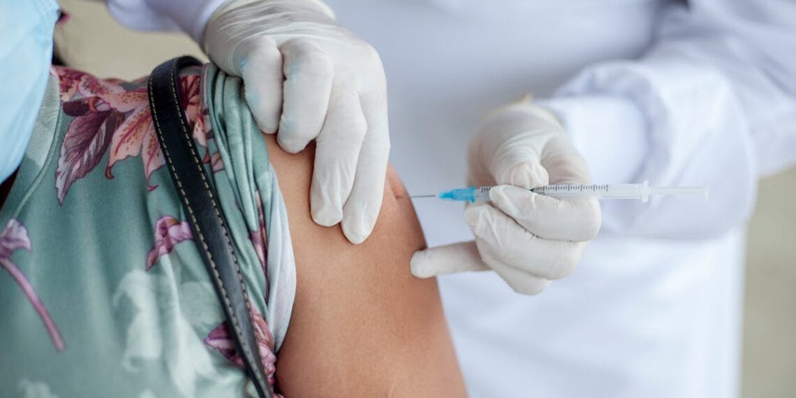 Close-up of a healthcare professional giving a vaccine shot to a patient wearing a mask.