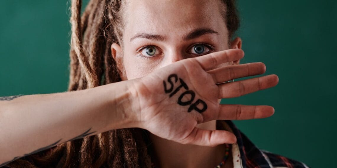Close-up of a woman holding her hand marked with 'stop' in front of her face, symbolizing protest and strength.