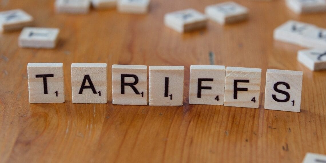 Scrabble tiles standing upright on a wooden table to spell tariffs