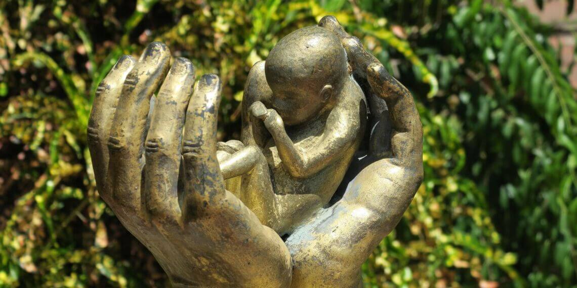 Sculpture of a baby between 2 hands