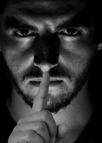Dark photo of man with finger to his lips symbolizing censorship by microsoft
