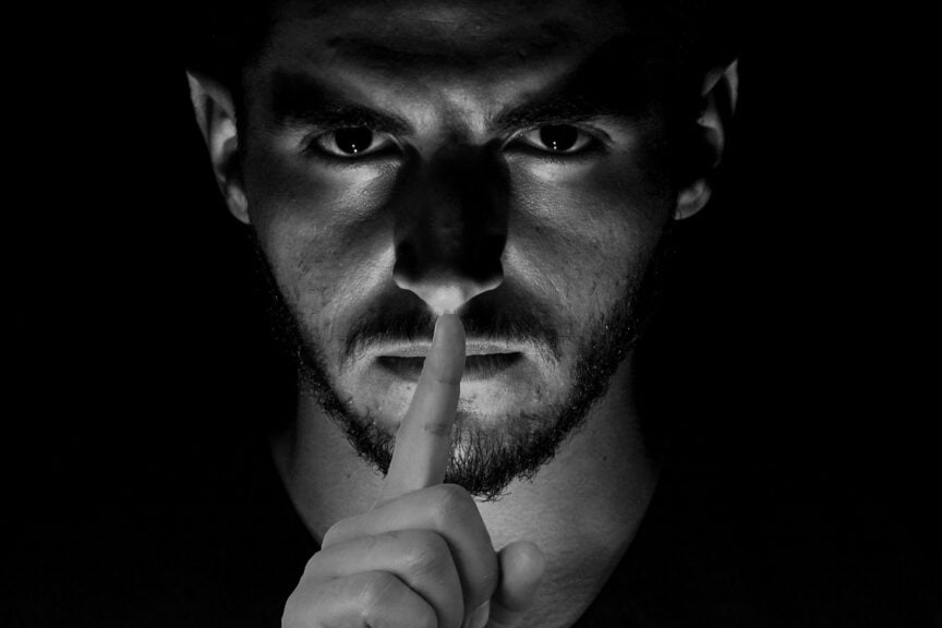 Dark photo of man with finger to his lips symbolizing censorship by microsoft
