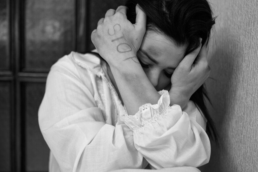 Victim of domestic violence. A woman crouched down, shielding her face with bruises on her arm.