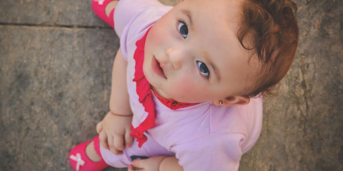Cute toddler wearing pink, captured from above, gazing up with innocence and curiosity